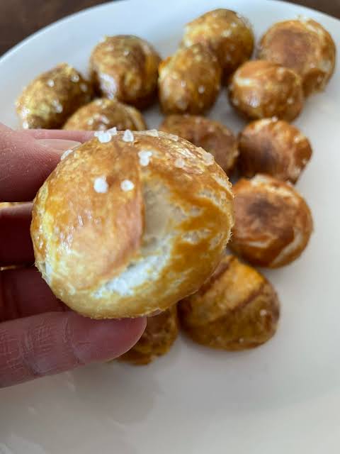 Hand holding a salted pretzel bite above a plate of more bites.