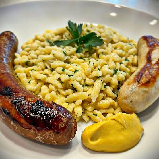 Two grilled sausages served with short pasta, chopped herbs and mustard.