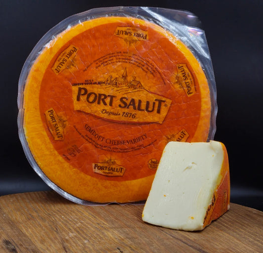 Port Salut cheese wheel with a piece on a wooden board against a dark background