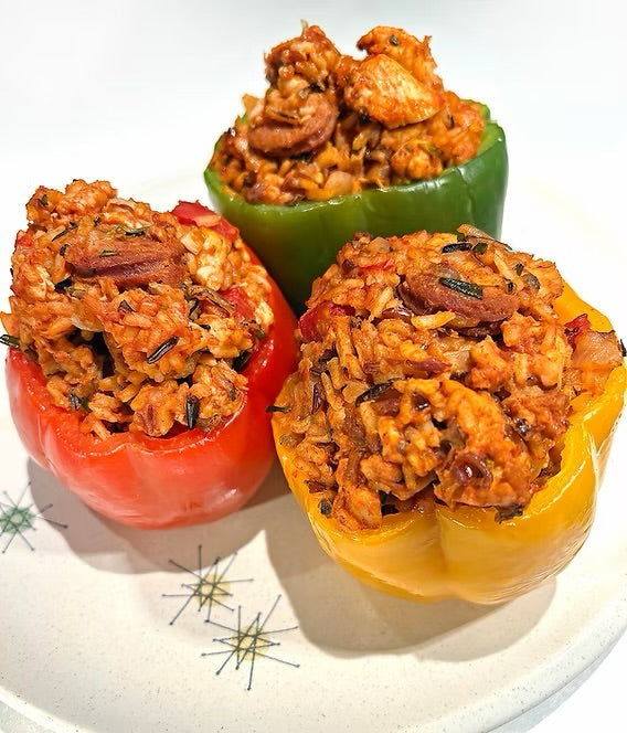 Three stuffed bell peppers in red, green, and yellow, filled with seasoned rice ground chicken chorizo and topped with chicken, arranged on a white plate.