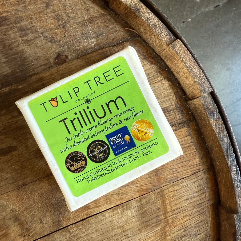 A package of Tulip Tree Creamery Trillium triple cream bison-milk cheese resting on a rustic wooden barrel surface.