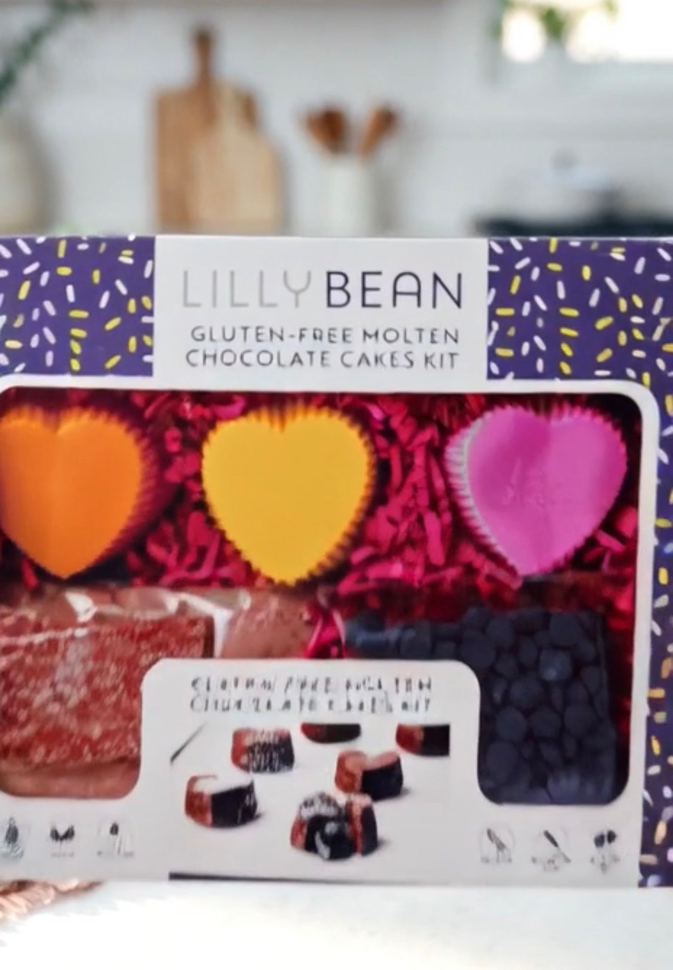 Lilly Bean Gluten-Free Molten Chocolate Cakes Kit box, showing the purple branded packaging with a clear window displaying colorful heart-shaped chocolates and chocolate chips.