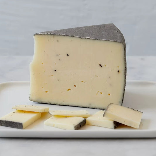 A wedge of creamy off-white cheese with a dark gray rind, shown on a white serving platter with several cut slices in front.