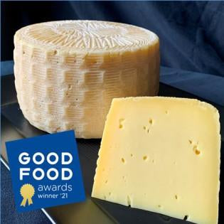 Round of Milkweed cheese with a slice on a dark surface, featuring the Good Food Awards logo.
