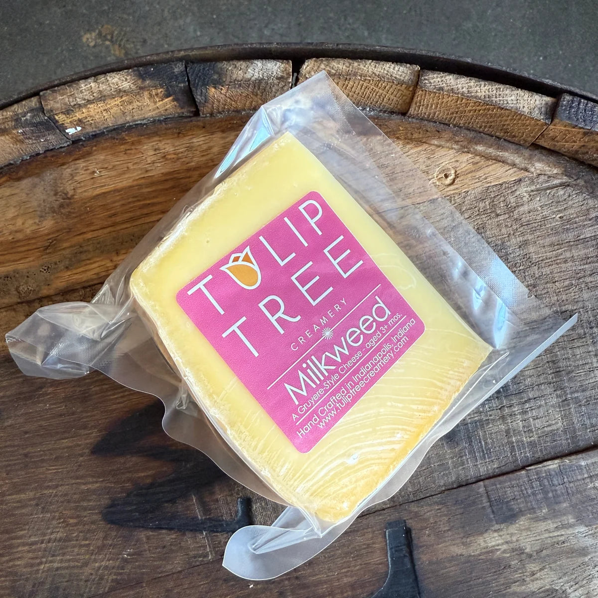 A vacuum-sealed wedge of Tulip Tree Creamery Milkweed cheese resting on a rustic wooden surface.