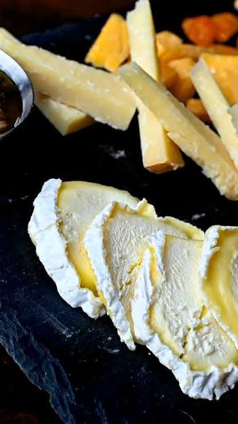 Slices of Milkweed cheese with yellow centers arranged on a dark slate platter, with additional cheese wedges in the background.