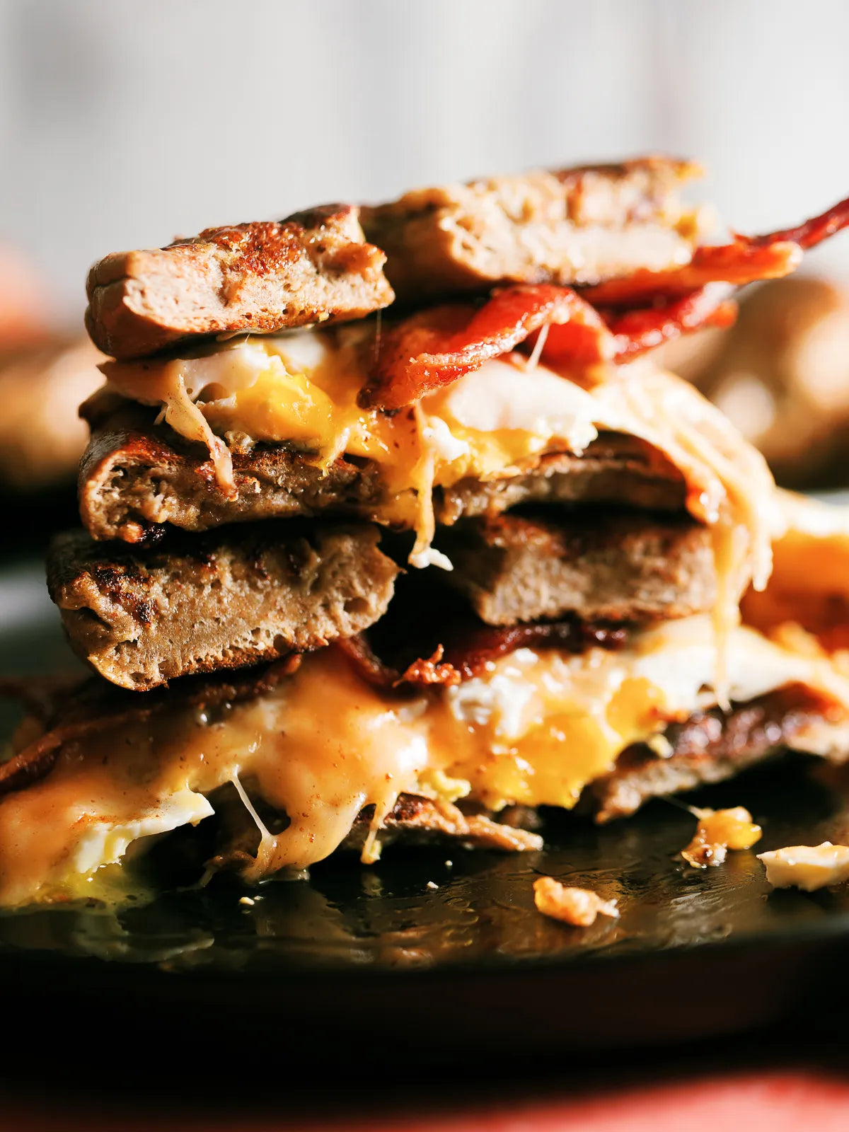 A close-up shot of a stacked  grilled cheese sandwich on a dark plate, featuring toasted bread, melted pumpkin spice gouda cheese, bacon, and a fried egg.