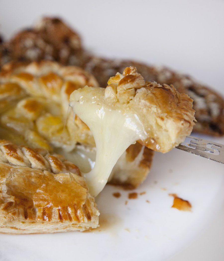 A close-up of a cheesy baked pastry or pie crust on a white plate, with a fork lifting a piece that shows a long stretch of melted cream cheese.