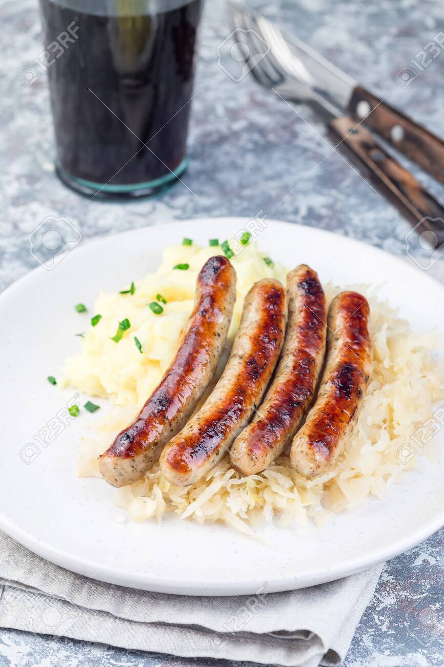 Four grilled bratwurst links over sauerkraut on a white plate.