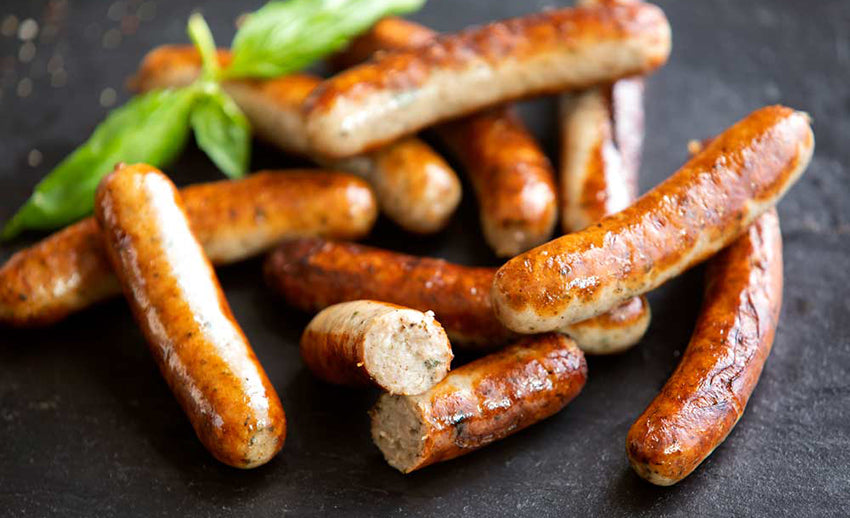 Browned bratwurst links on a dark surface, with one cut open to show the filling.