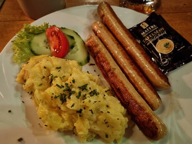 Three browned bratwurst links served with potato salad, lettuce, cucumber and tomato.