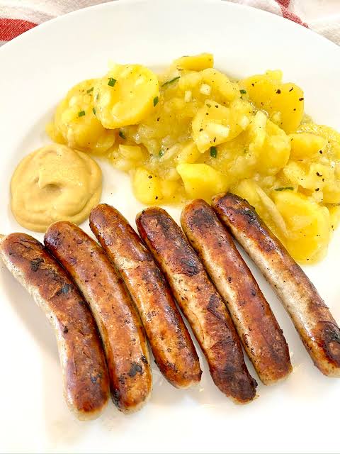  Four grilled bratwurst links over sauerkraut on a white plate.
