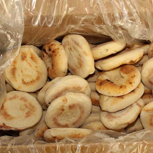 A pile of round bialy bagels, toasted flatbread or bread rolls partially visible inside a clear plastic-lined container.