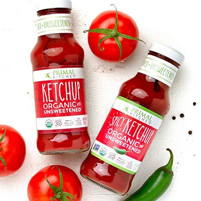 Two bottles of Primal Kitchen ketchup with tomatoes and a jalapeño pepper on a white background
