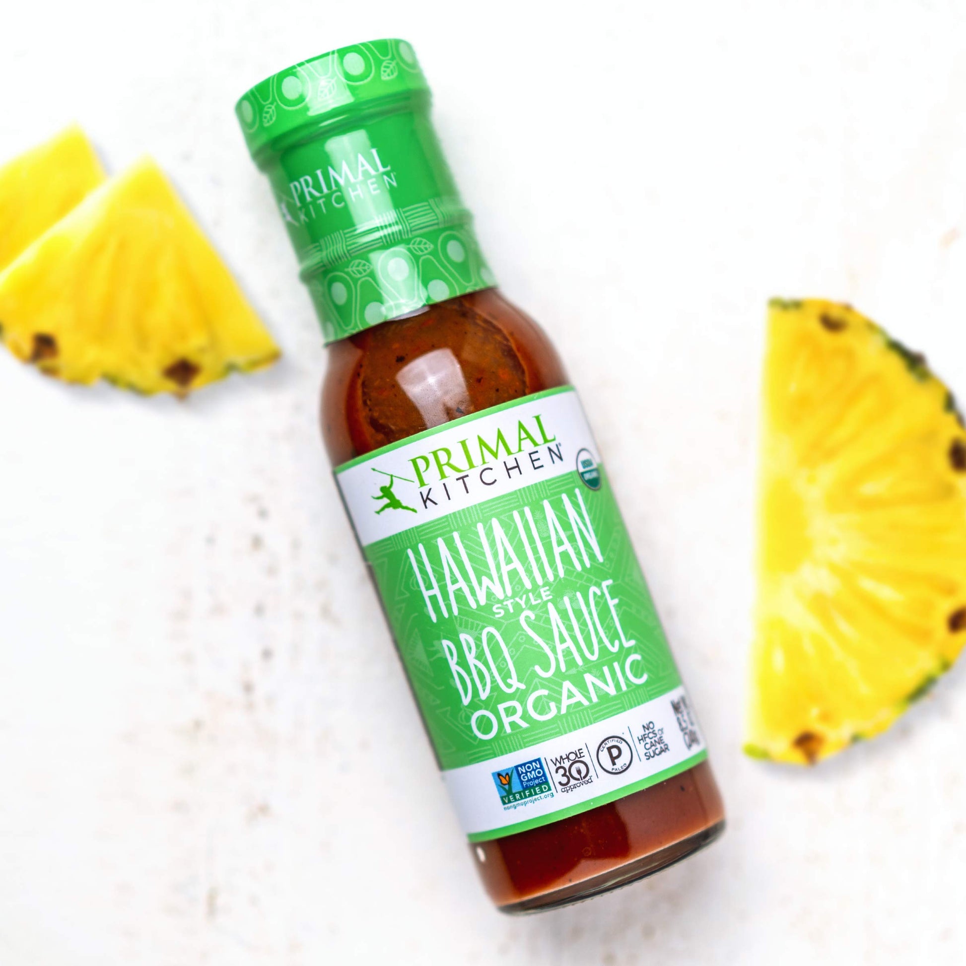 Bottle of Primal Kitchen Hawaiian Style BBQ Sauce with pineapple slices on a white background