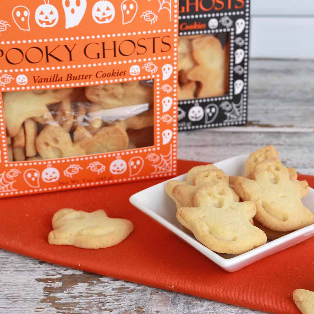 Halloween-themed vanilla butter cookies shaped like ghosts, shown on a white plate with orange packaging boxes in the background.