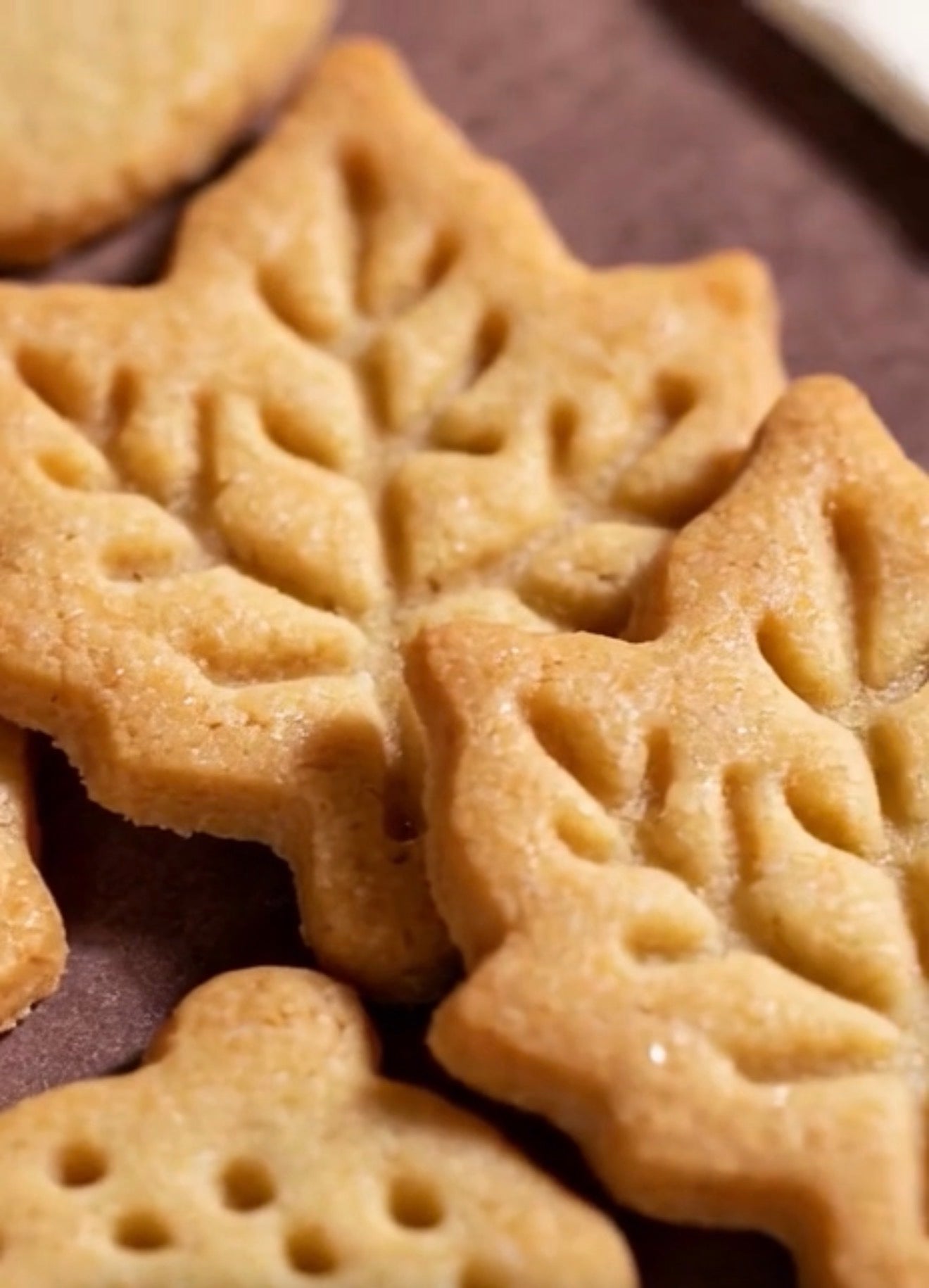 Close-up of several golden-brown leaf-shaped cookies stacked on a dark brown surface.