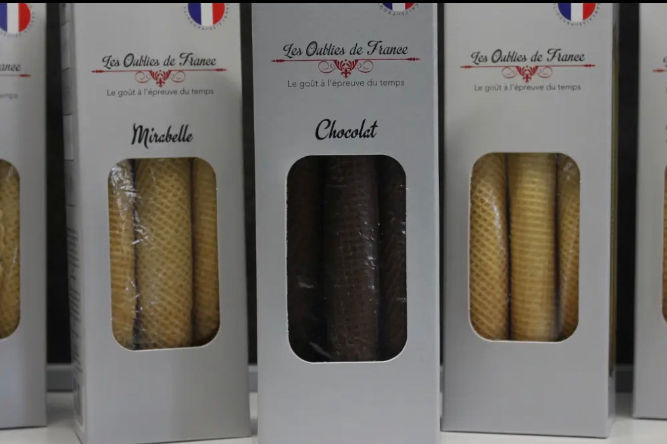 Three white boxes of Les Outils de France chocolate waffle sticks lined up on a white surface. The center box is labeled 'Chocolat' and shows dark brown waffles through a clear window, while the side boxes are labeled 'Mislabelle' and show golden-yellow waffles.