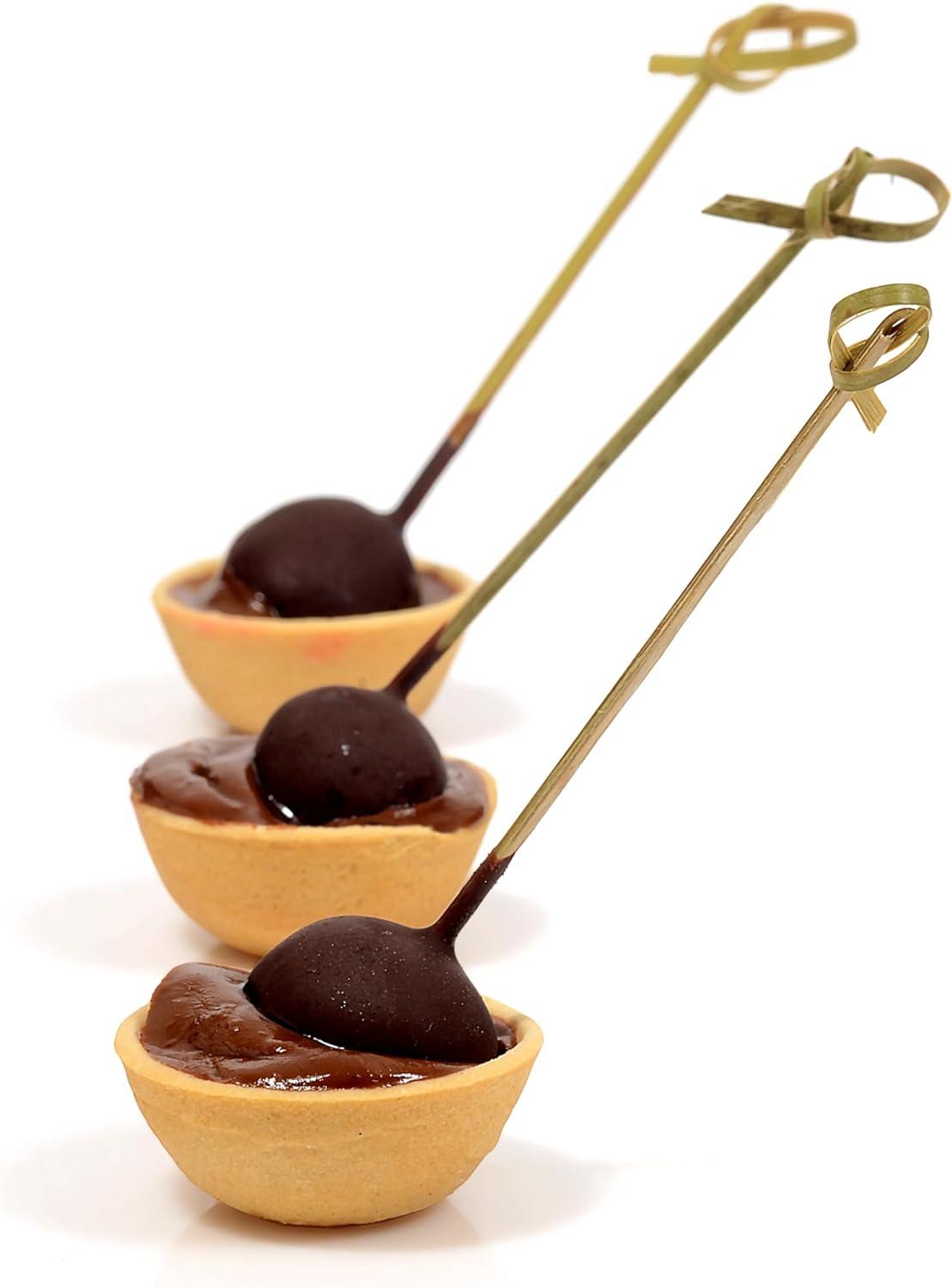 Three mini chocolate tartlets with dark chocolate spheres on skewers, arranged diagonally on a white background.