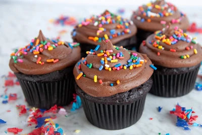 Chocolate cupcakes with chocolate frosting and colorful sprinkles on a white surface.