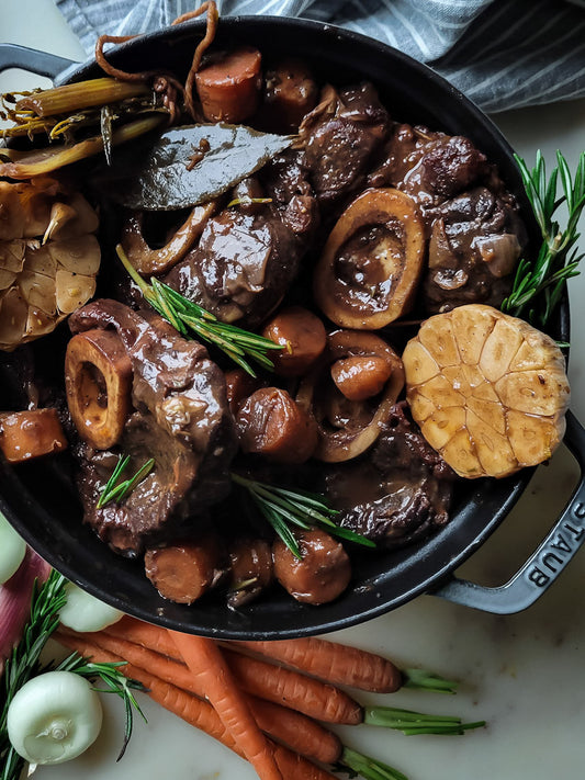 Stew with beef bones, vegetables, and herbs in a pot on a marble surface.