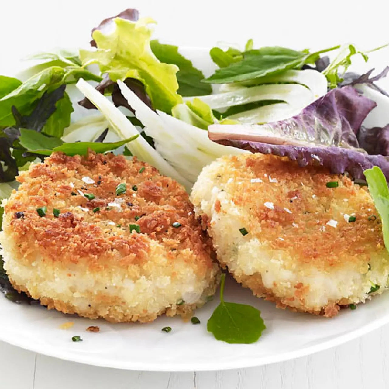 Two golden-brown breaded fish cakes served on a white plate with a fresh green salad.
