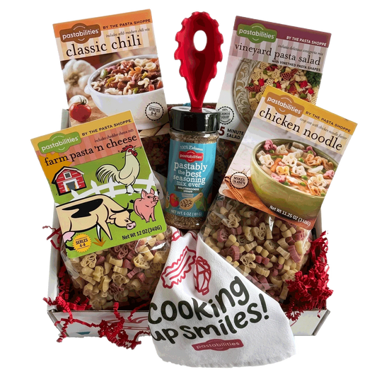 A gift basket filled with pasta products from Pastabilities, including Classic Chili, Vineyard Pasta Salad, Farm Pasta 'n Cheese, and Chicken Noodle, along with a jar of best seasoning and a white bag reading 'Cooking up smiles!'.