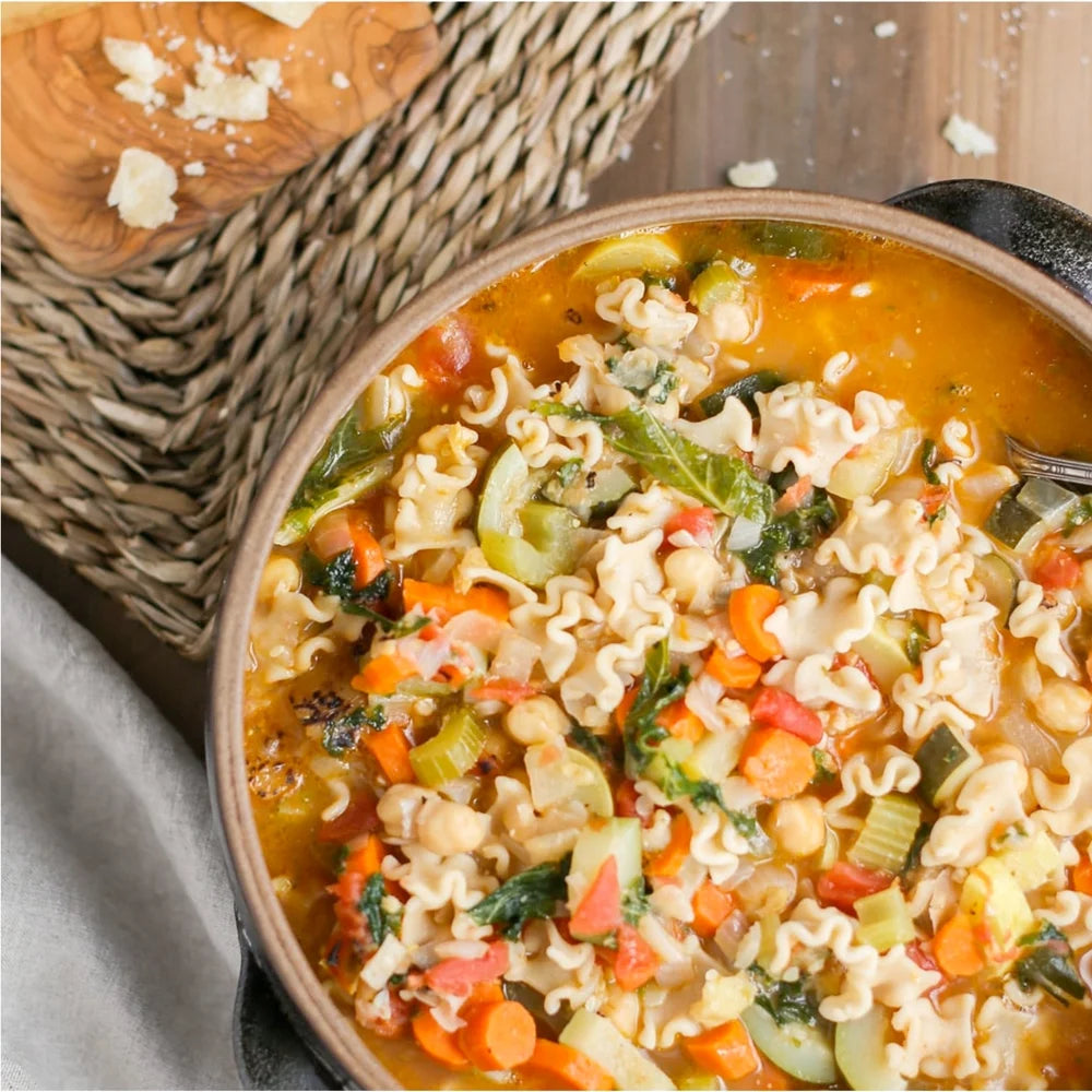Bowl of vegetable soup with pasta and carrots, placed on a woven mat.