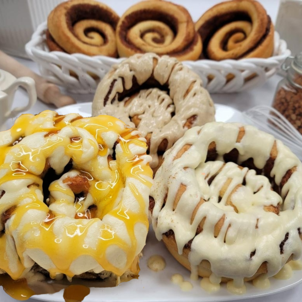 Three frosted cinnamon rolls arranged on a white plate, with two more in a white basket in the background. The front rolls are topped with bright yellow drizzle, and the center roll has a light beige drizzle.