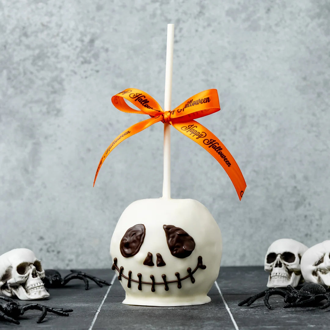 Jack Skellington Chocolate Caramel Apple  White chocolate-covered apple with a Halloween-themed ribbon on a gray background