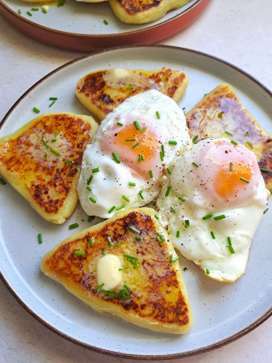 A close-up of a plate of breakfast Irish potato bread cakes with two sunny eggs, chives, and butter on a light beige plate.