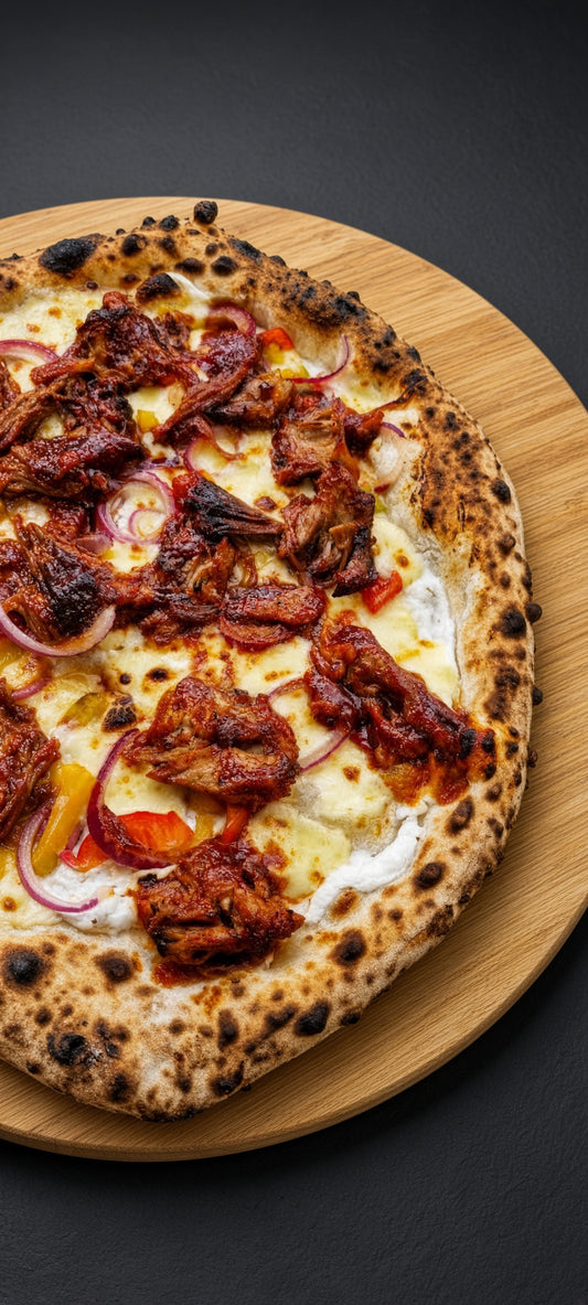 A close-up overhead shot of a freshly baked pizza on a round wooden board against a dark background. The pizza has a charred, blistered crust with dark spots, topped with melted cheese, pieces of grilled meat, red onion slices, and small pieces of bell pepper.