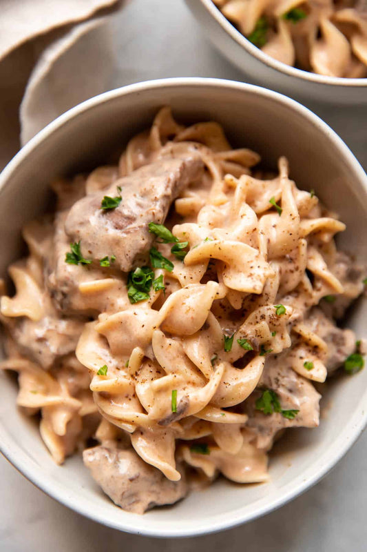 Bowls of creamy pasta with meat and herbs on a light background
