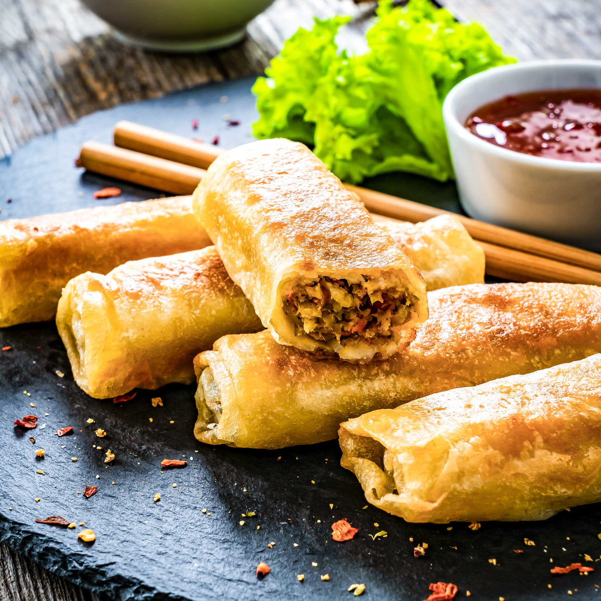 Egg rolls on a black slate plate with dipping sauce and chopsticks.