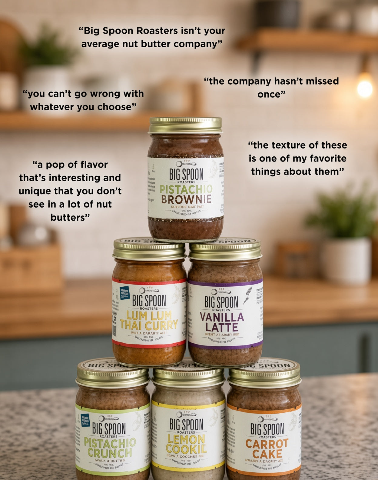 A pyramid arrangement of Big Spoon Roasters nut butter jars on a kitchen countertop, with several quote overlays around the product. The central stack includes Pistachio Brownie, Lum Lum Thai Curry, Vanilla Latte, Pistachio Crunch, Lemon Cookie, and Carrot Cake.