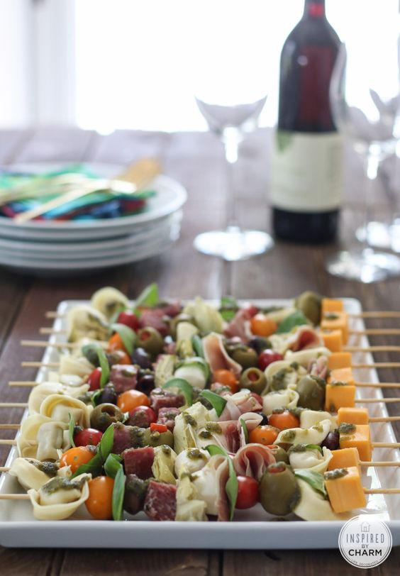 Pasta skewers on a platter with a bottle of wine and glasses in the background.
