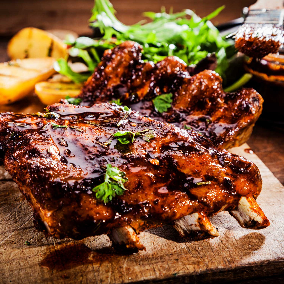 Grilled ribs with barbecue sauce on a wooden cutting board, surrounded by vegetables.