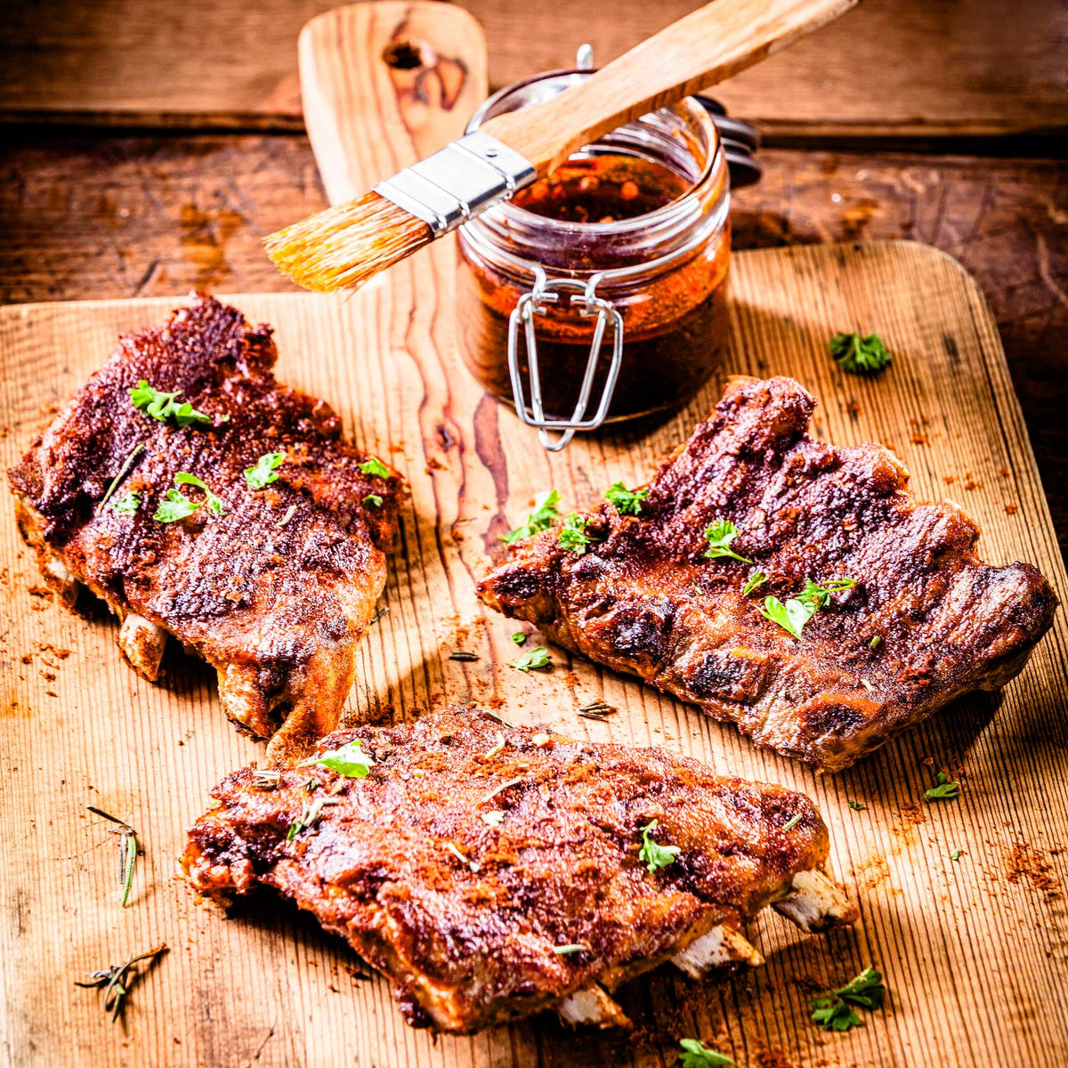 Barbecued ribs on a wooden cutting board with a jar of sauce and brush.