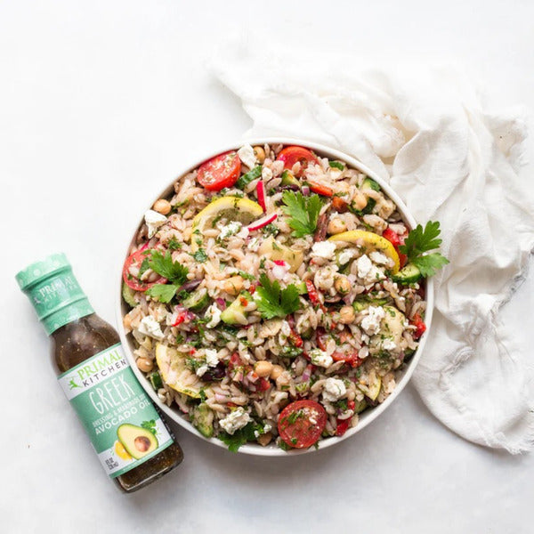 Colorful salad with vegetables and a bottle of dressing on a white surface