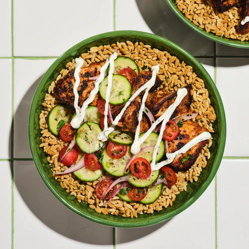 Bowl of salad with grilled chicken, cucumbers, tomatoes, and rice on a green plate.