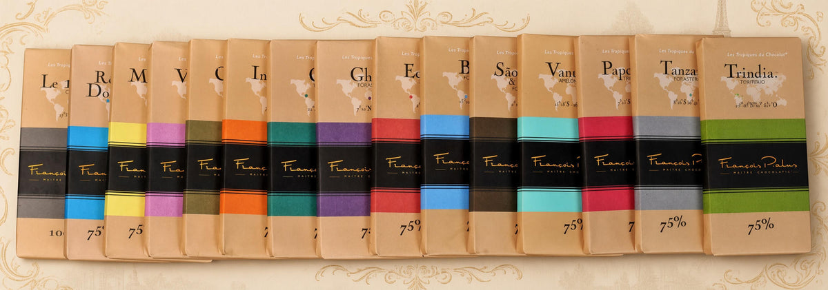 Row of François Pralus single-origin dark chocolate bars in kraft paper wrappers with colored bands, arranged in a fan shape showing the full range of origins