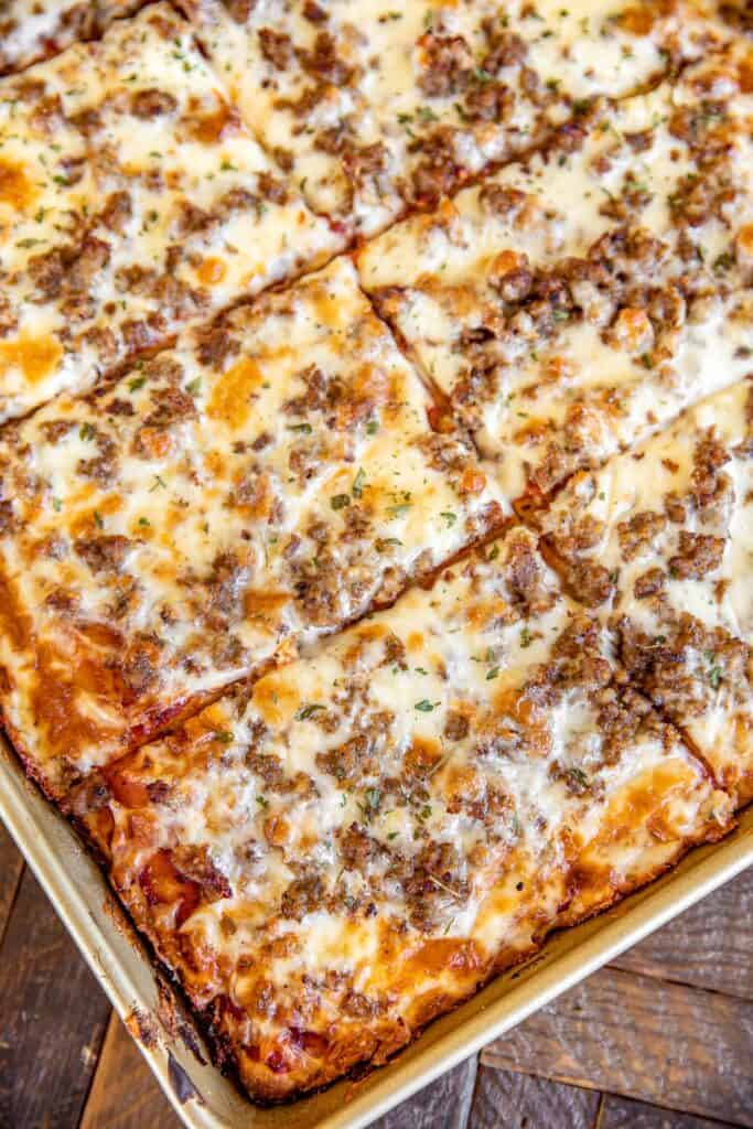 Sliced cheesy baked pasta dish in a metal baking pan on a rustic wooden surface.