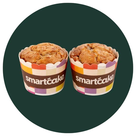 Two golden-brown smartcake muffins in branded paper cups, centered inside a large dark green circular frame on a white background.