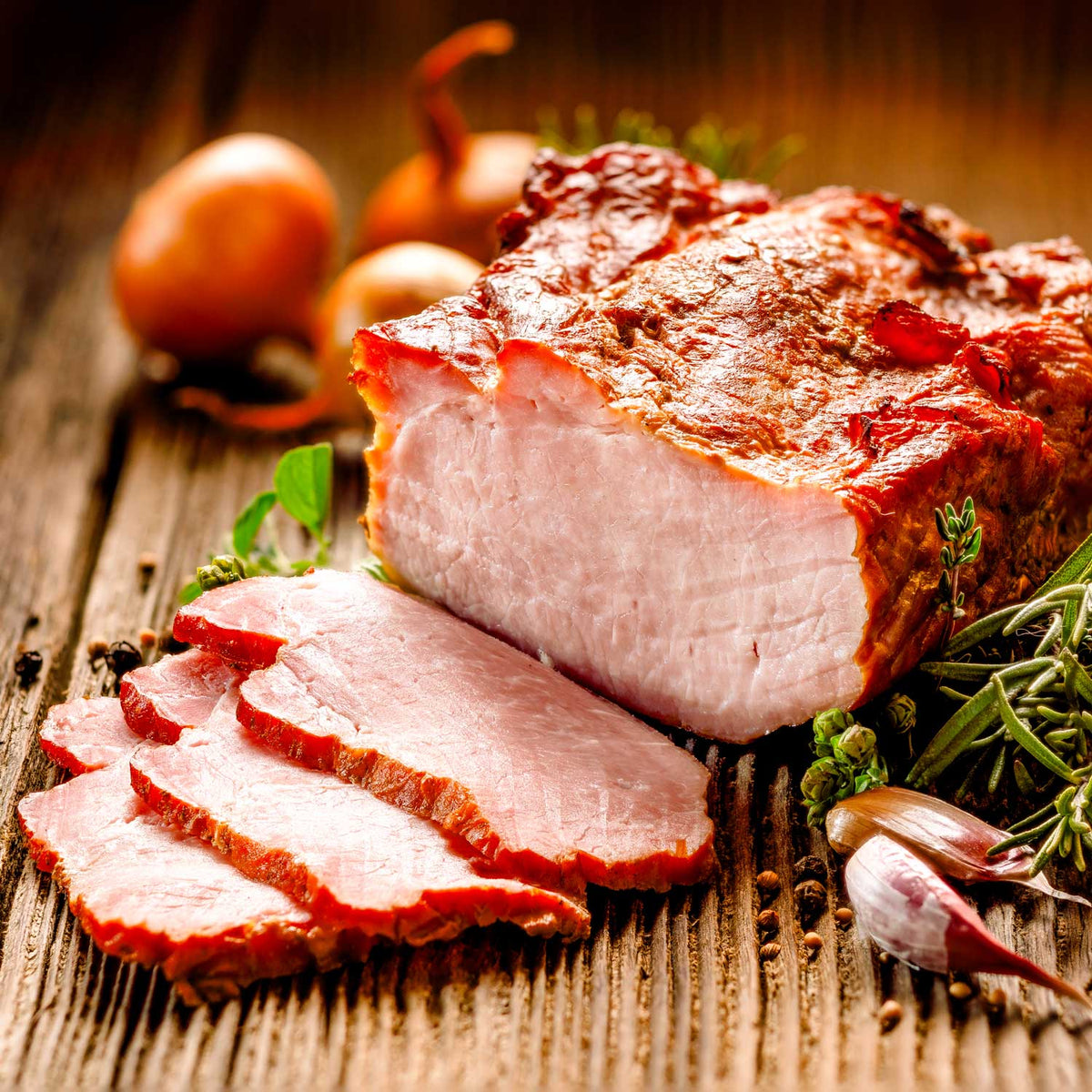 Sliced roasted pork with herbs and onions on a wooden surface